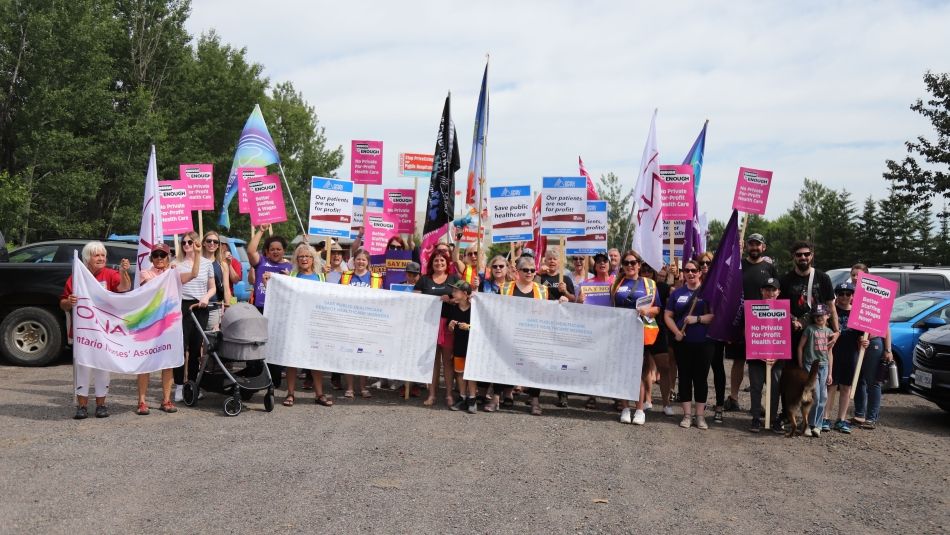 Rassemblement à Thunder Bay : un grand groupe brandit des pancartes, des bannières et des drapeaux roses, blancs, bleus et rouges.