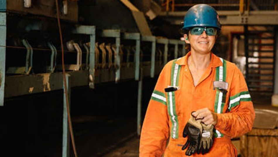 Trades women wearing a hard hat, safety glasses and orange overalls