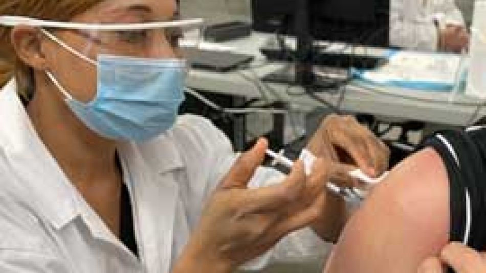 A nurse wearing PPE putting a needle vaccine in an arm