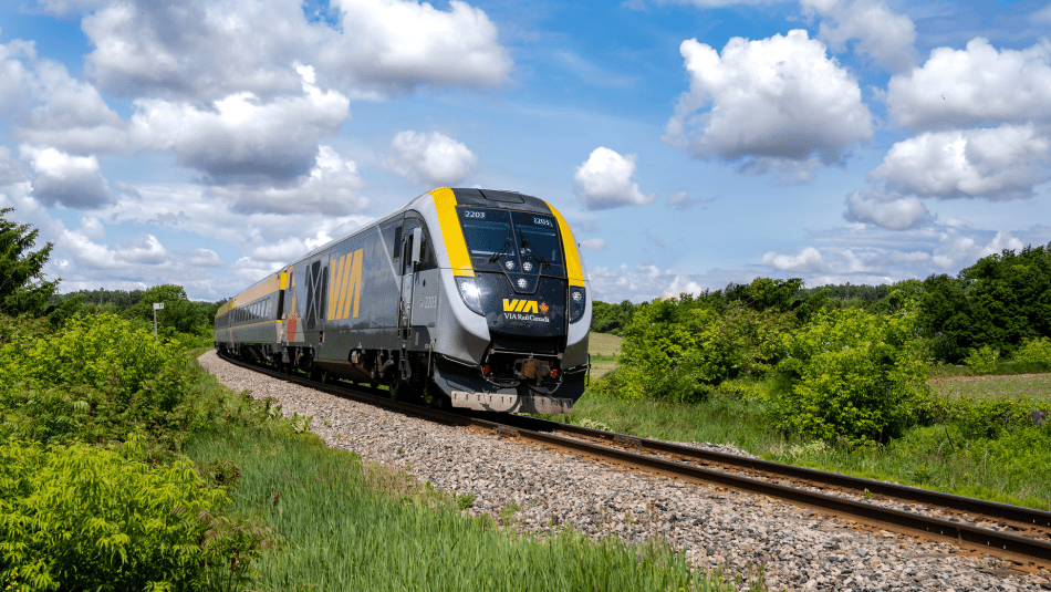 VIA Rail train going down the track on a sunny day through a vally with a blue cloudy sky