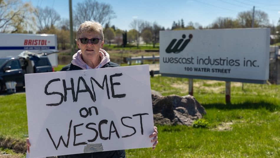 Laura Collison, employée de Wescast, tient une pancarte sur laquelle on peut lire « Honte à Wescast » devant une enseigne de Wescast Industries Inc. à Wingham, en Ontario.