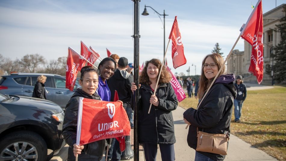 Women carrying Unifor flags gather in a group.