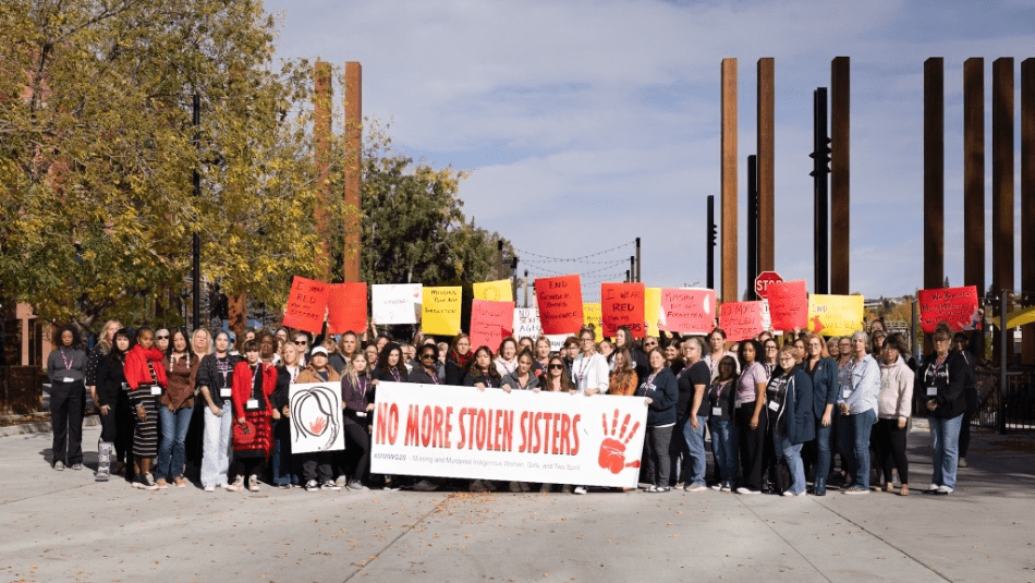 A large group of women hold a banner "No more stolen sisters" and coloured placcards up high