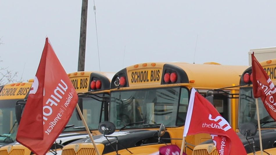 Line of parked school buses with Unifor flags in front