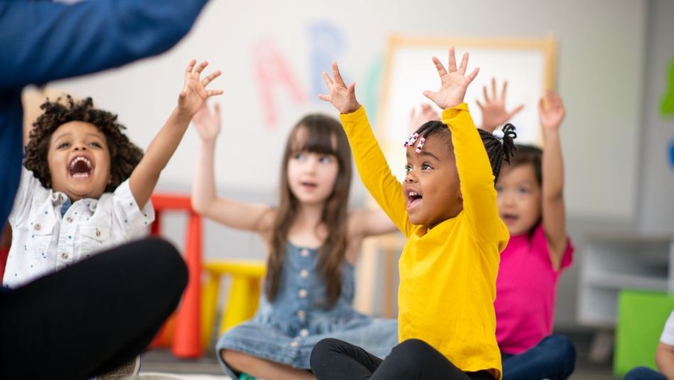 children laughing sitting on the floor with their arms up 