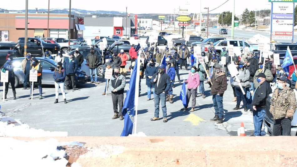 Large group gathering outdoors holding flags and placards in a parking lot