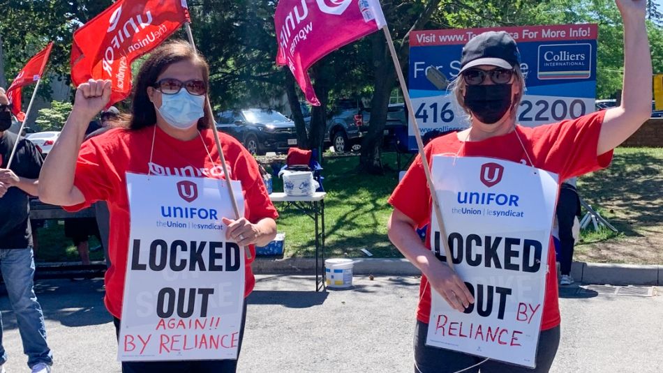 Two women on a picket line wearing 'locked out' placards with fists in the air