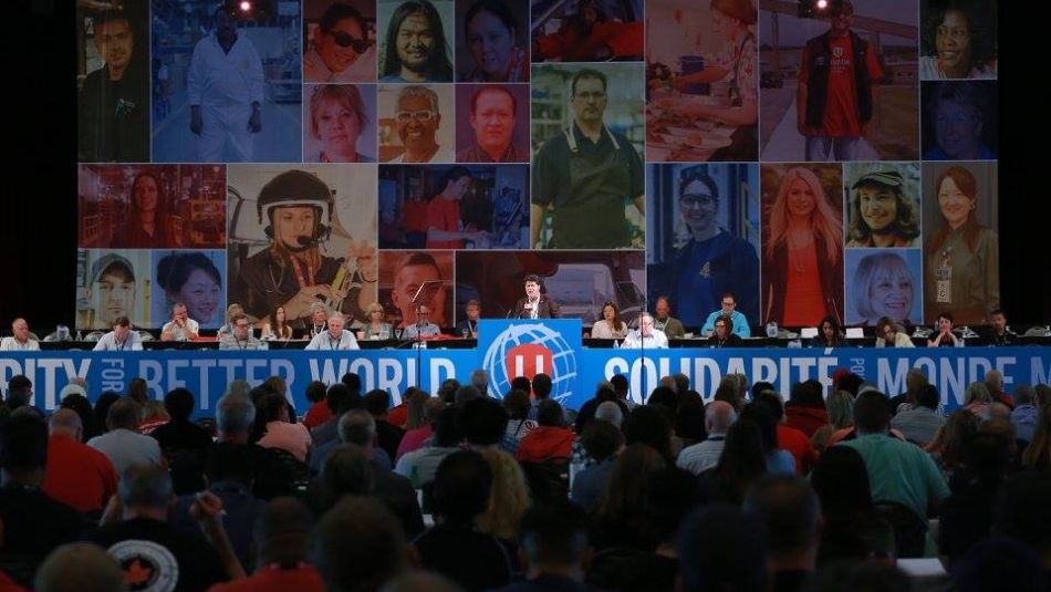 The head table at Canadian Council, in front of a large backdrop showing portraist of dozens of Unifor members in their workplaces.