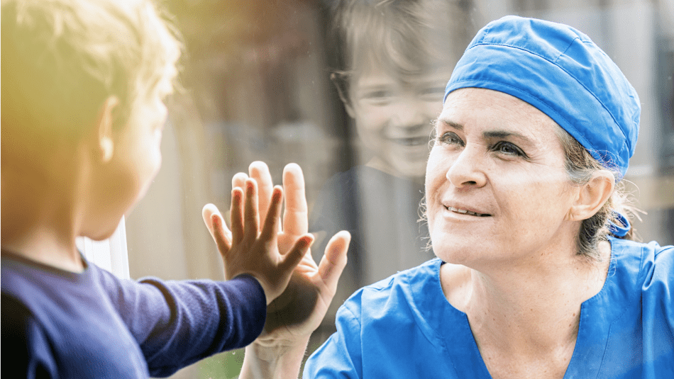 a nurse and a child touching hands through a glass window