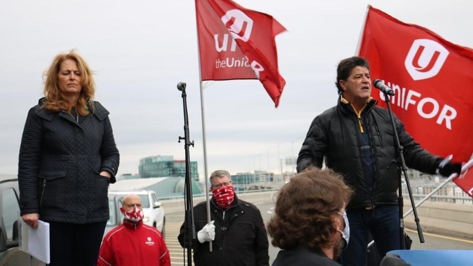 Jerry Dias with Katha Fortier speaking at a mic to a rally Unifor flags