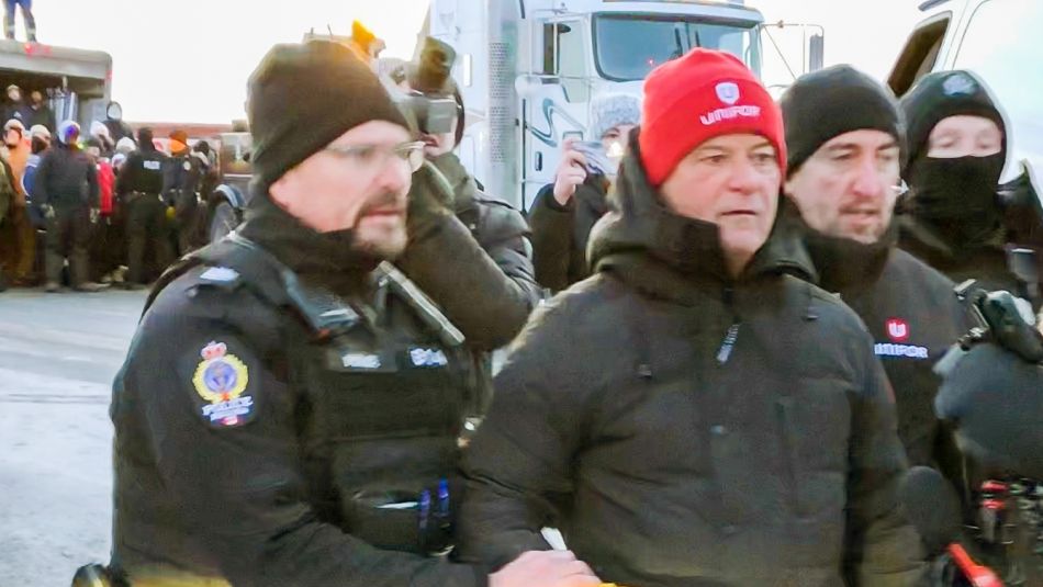 Jerry Dias and Gavin McGarrigle being escorted by police officers outdoors after arrest.