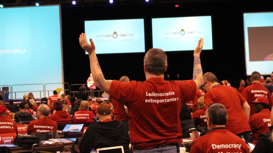 Vue de derrière, une salle pleine de membres d'Unifor portant des t-shirts identiques lisants « La démocracie est importante! »