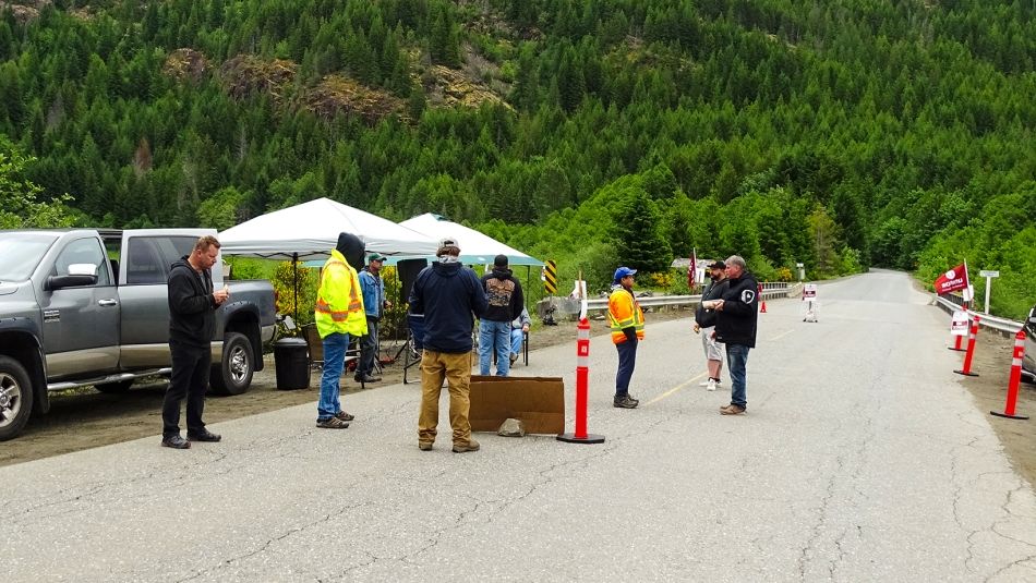 A dozen people stand on the road at a remote picket line location with forested mountains in the background