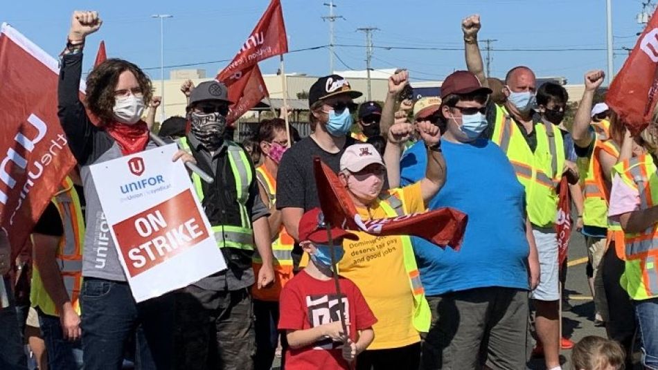 Members of Local 597 stand on a picket line holding flags and strike signs.