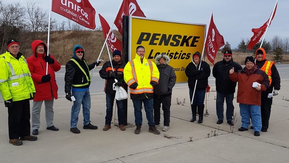 Unifor members wave flags in front of a Penske Logistics sign.