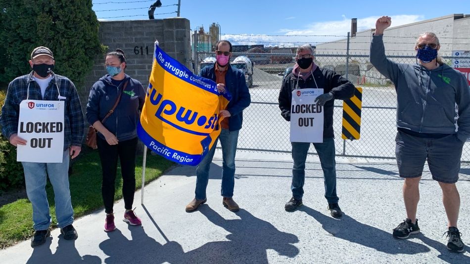 "People standing on a picket line with "locked out" placards and flags."