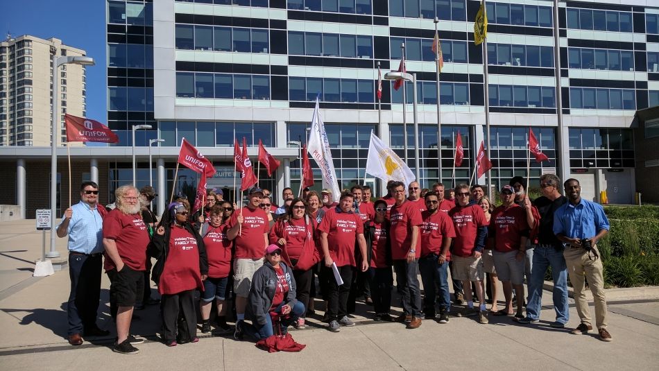 A few dozen Unifor members who work in retail wearing matching shirts and holding flags outside Peel  regional offices.