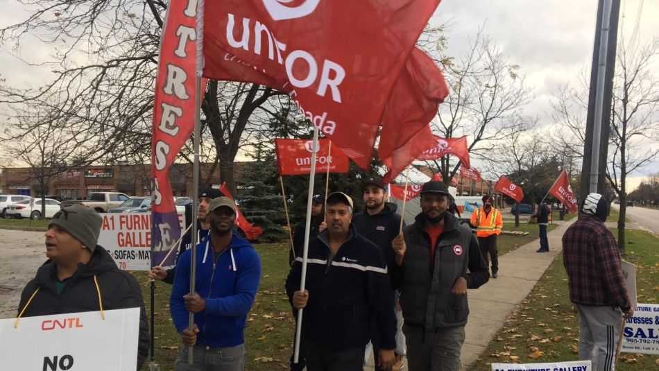 Members of Unifor Unifor Local 4003 carry flags on a picket line.