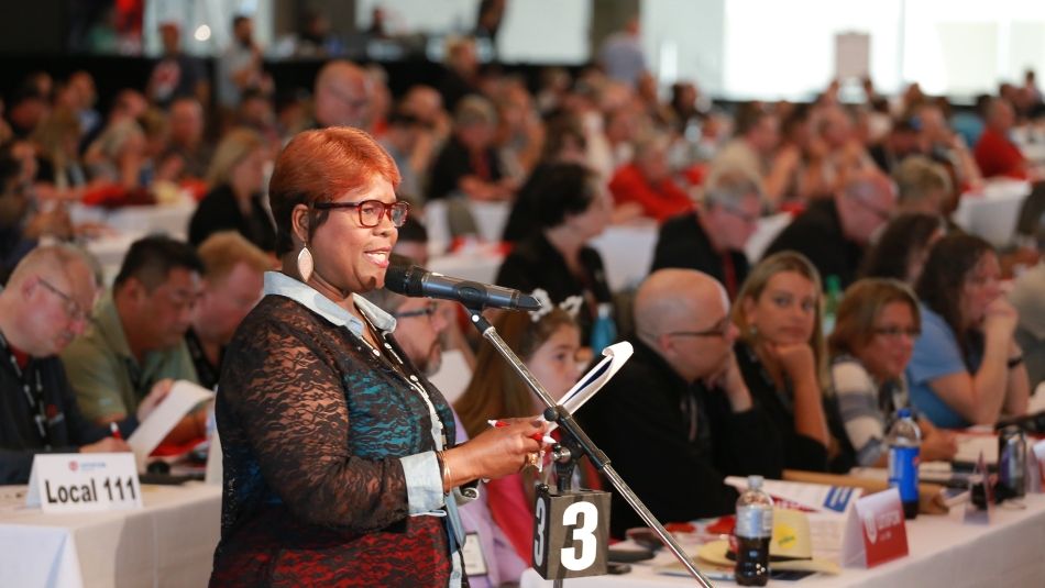 A delegate to Canadian Council addresses other delegates at a microphone.