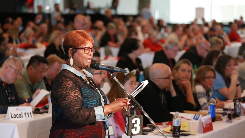 A delegate to Canadian Council addresses other delegates at a microphone. 