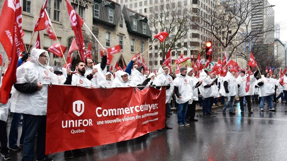 Unifor activists in matching rain ponchos hold flags and a banner at a rally in Montreal.