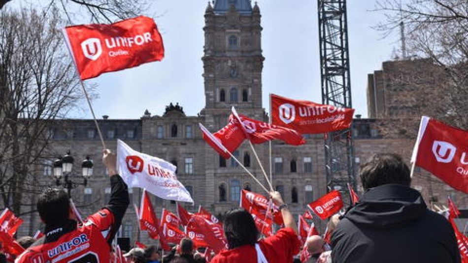 Vu d'arriere, des membres d'Unifor brandissent des drapeaux lors d'un rassemblement sur la colline du Parlement à Québec.