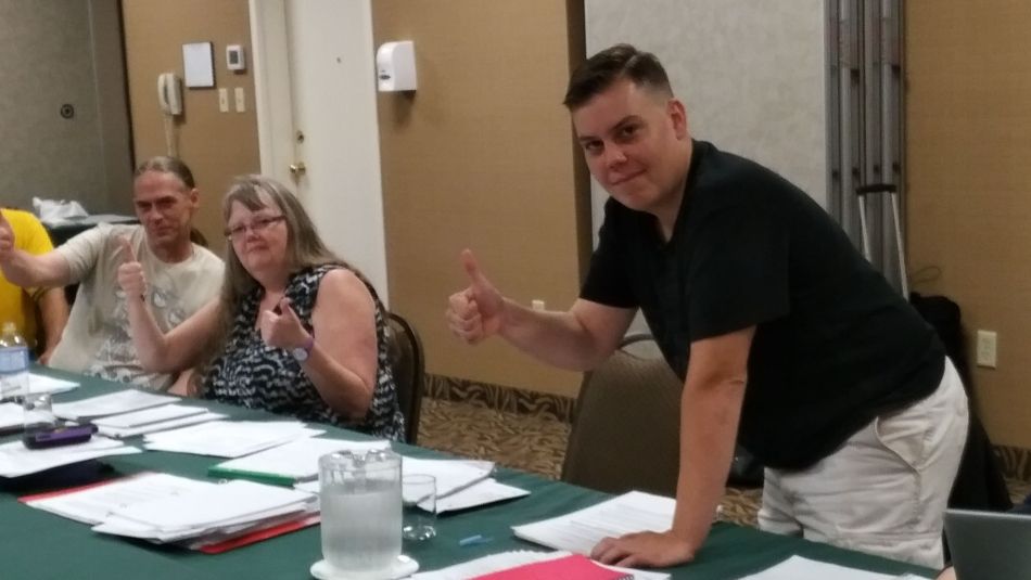Members of the Local 4612 bargaining committee, seated at a long table, give thumbs up.