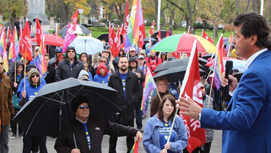 Jerry Dias speaks to a crowd holding Unifor flags and umbrellas.