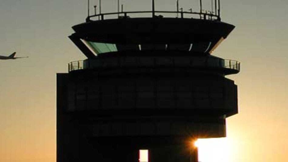An airplane flys past an air traffic control tower.
