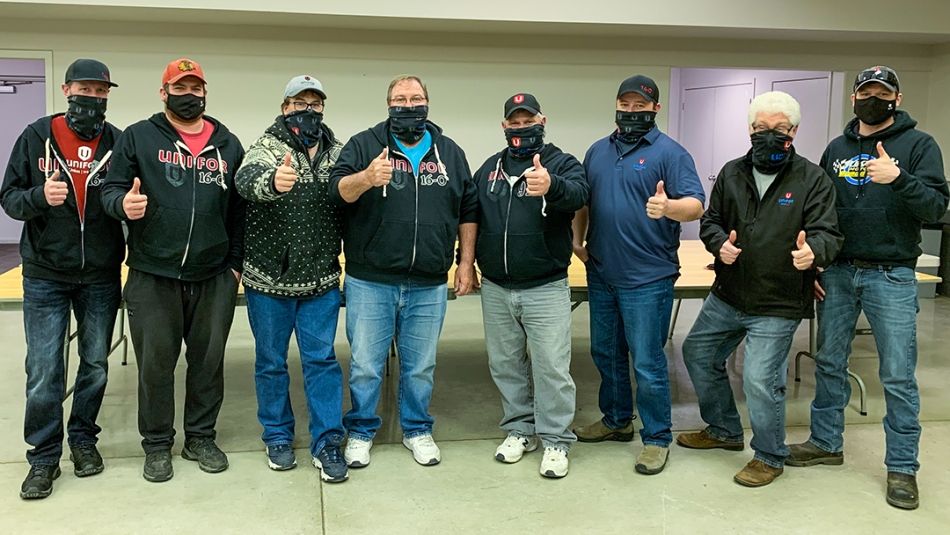 Photo of eight miners in casual clothing and masks giving the thumbs up