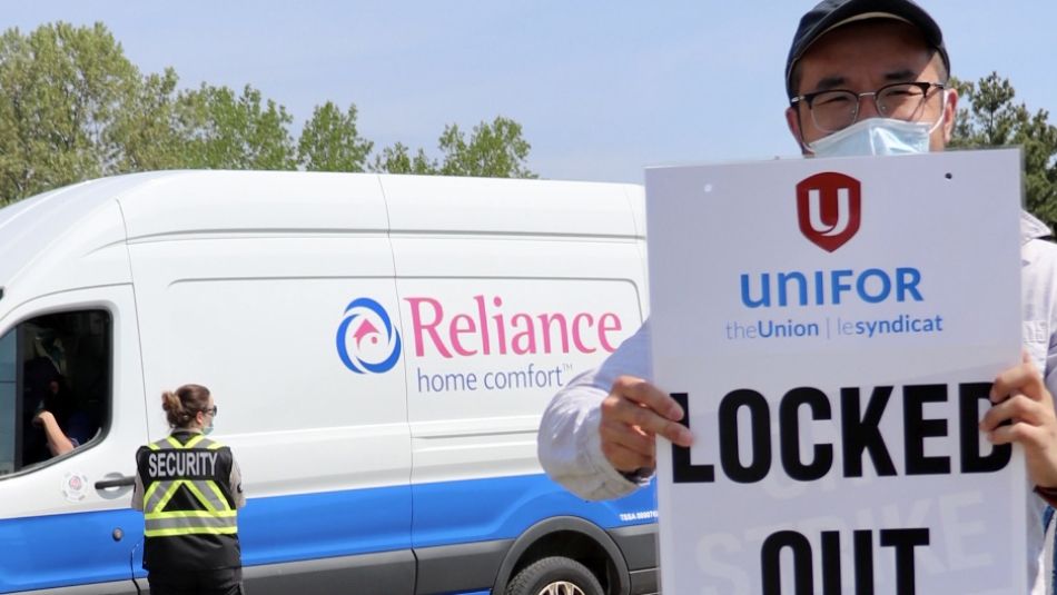 Worker holding a 'locked out' sign in front of a van crossing a picket line