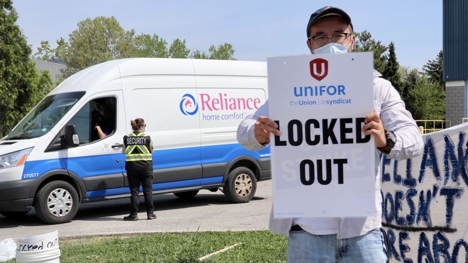 A member standing in front of a Reliance Home Comfort work van holding a Locked Out sign with a Unifor logo