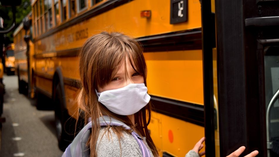 A masked student boards a school bus.