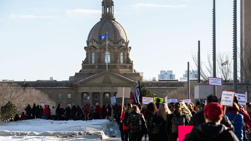 Photo of demonstrators with placards marching up Alberta legislature lawn in winter