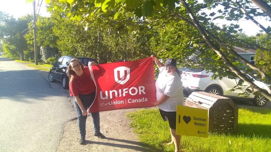 Two Unifor members hold up a Unifor flag next to a sign reading: "I love Dominion workers."