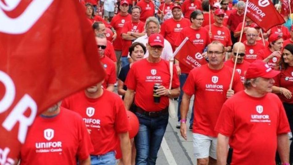 A large crowd of workers march wearing Unifor red t-shirts.