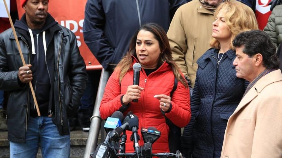 Pre-pandemic photograph of Naureen Rizvi speaking at a microphone at a rally for workers’ rights. 