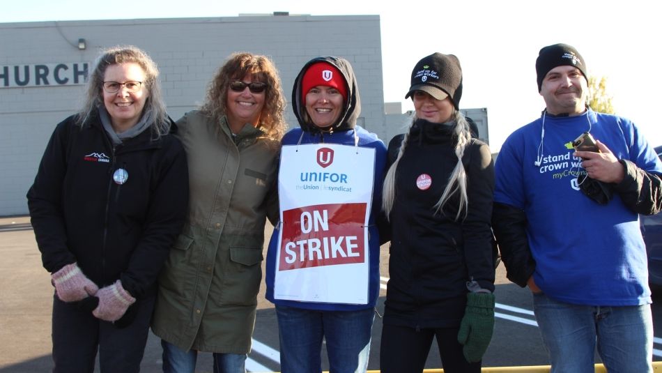 Five Unifor members stand on a picket line.
