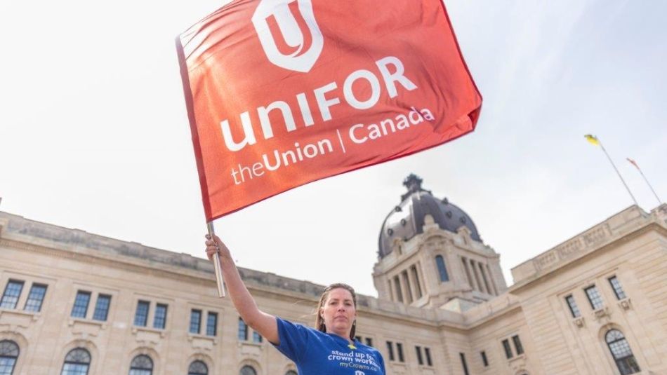 A Unifor member stands in front of the Saskatchewan legislature hold a red flag in the air.