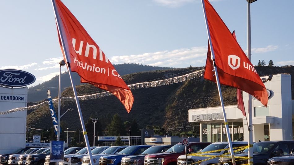 Two Unifor flags fly in front of the Dearborn Ford dealership.