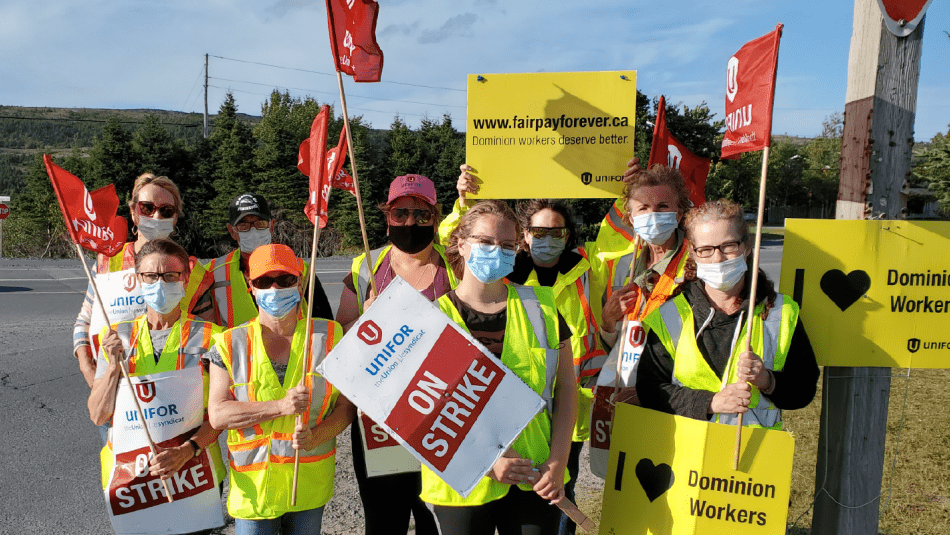 A group of Unifor Local 597 members wearing masks hold Unifor flags and strike signs.