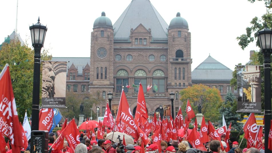 A large crowd of activists carry Unifor flags outside Queen's Park in Toronto, On.