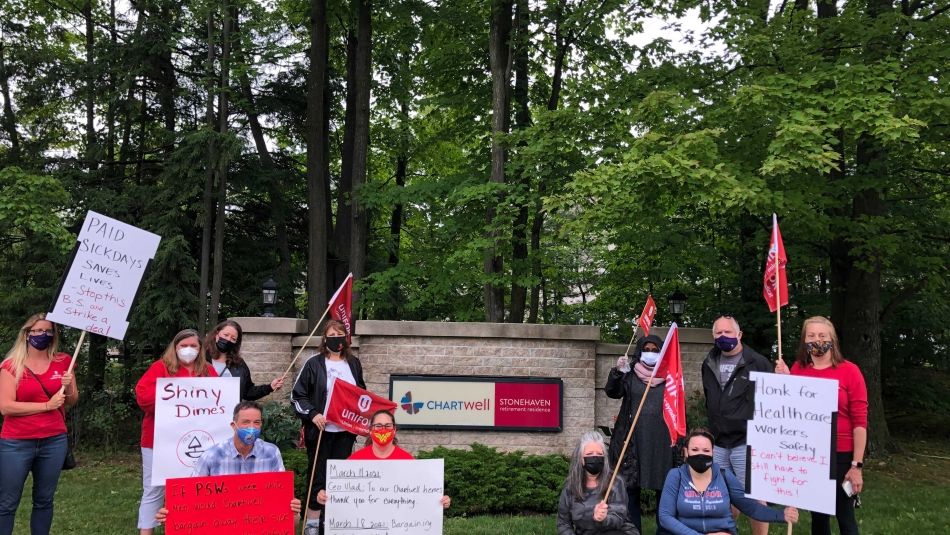 Health care workers at a rally in front of a Chartwell's sign outside on a decrative wall. Workers are holding signs and flages posing.