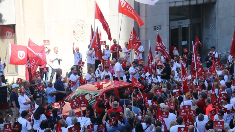 Jerry Dias speaks to a large crowd waving Unifor flags.