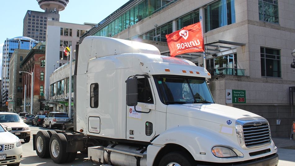 A transport truck flying a Unifor flag drives through the city.