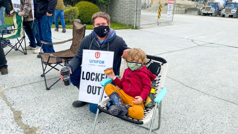 Photo of worker wearing a "Locked Out" sign posing with a young child at a picket line in Victoria, B.C.