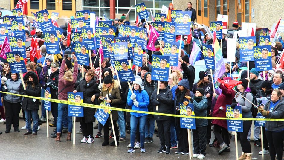 A crowd of Unifor members hold up signs shaming Saskatchewan premier Scott Moe.