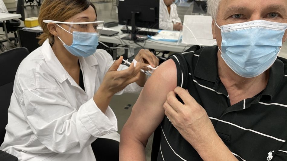 Nurse in mask and goggles administering a needle to the shoulder of a patient