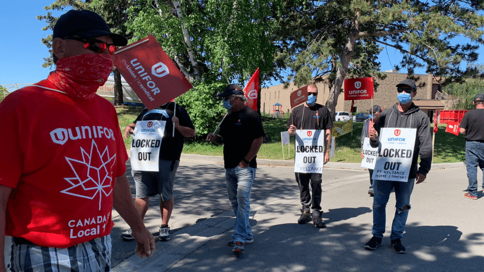 Five workers wearing "locked out" placards walk a picket line