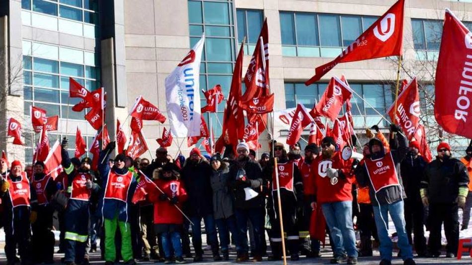 De membres d'Unifor agitent des drapeaux lors d'un rassemblement.